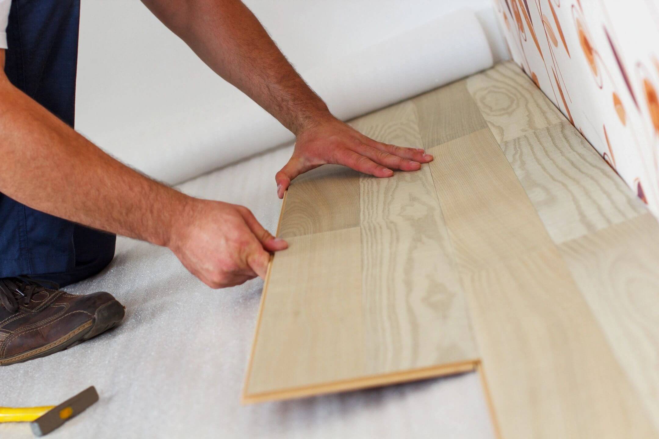 Person installing light wood flooring panels.