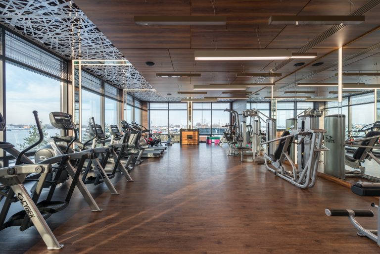 Modern gym with exercise machines and large windows.