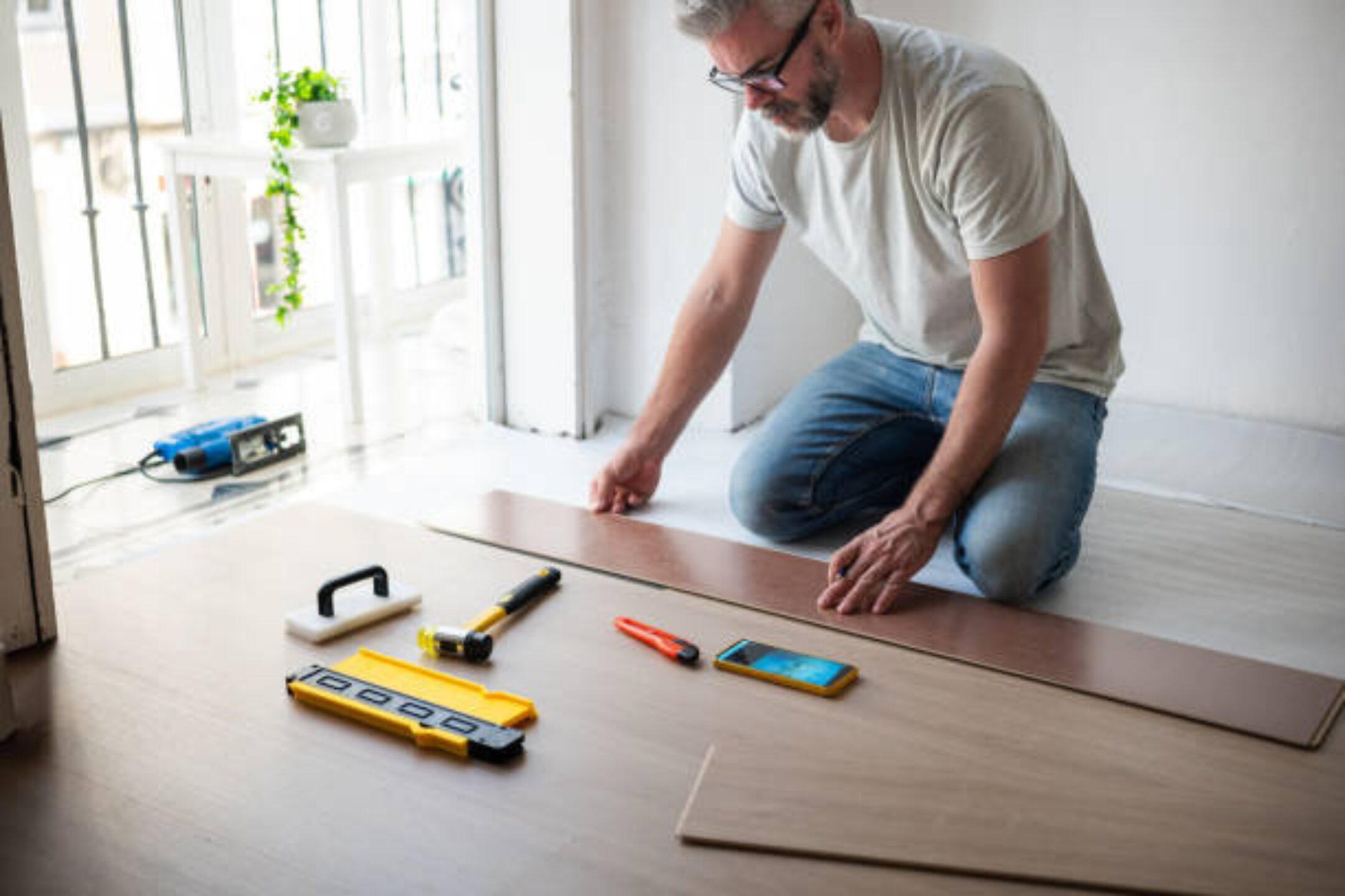 Man installing wooden flooring, tools nearby.